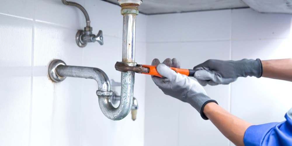 Plumber fixing a leaky bathroom sink pipe.