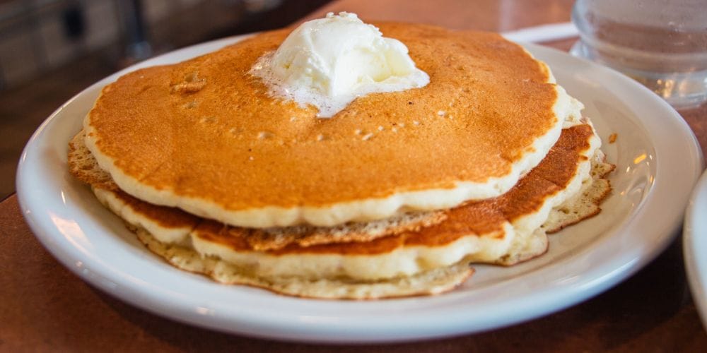 Soft stack of pancakes topped with butter on a white plate served in an american diner.